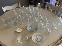 Top-down view of crystal glasses and dessert plates arranged on a round wooden table, displaying multiple sizes and styles of glassware with etched details.