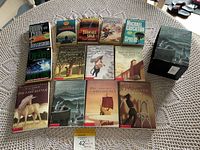 Photo of 15 novels including C.S. Lewis Narnia series and other popular novels by Robin Cook, Michael Crichton, and others arranged on a table.