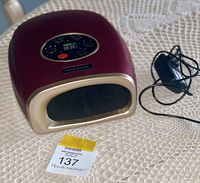 Front and side view showing the hand massager's main body, digital display, and remote control lying next to it.