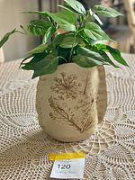 Front view of the pottery vase with botanical imprints and plant inside, placed on a crochet tablecloth.