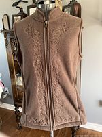 Brown fleece vest displayed on mannequin showing front embroidered design and full zipper.