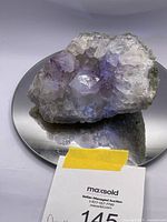Front angle of amethyst geode on round reflective base showing multiple purple crystal points and the natural stone exterior.