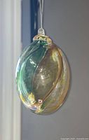Front view of the large glass ball showing green and amber swirling colors with hanging loop at top.