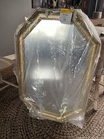 Front view of the large octagonal mirror with decorative beveled gold frame partially wrapped in plastic.