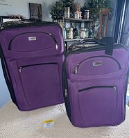 Two purple Tower brand upright suitcases shown standing on a table with front facing.