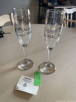 Two clear champagne glasses with printed gold and black text commemorating the Millennium year 2000 placed on a table next to a lot sticker.