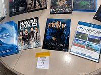 Photo showing four DVD and Blu-ray cases on a table, including Hawaii Five-0, Flashpoint season 3, HD Landscapes, and Epic Conditions.