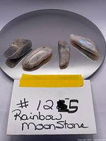 Four tumbled rainbow moonstones placed on a reflective surface, showing iridescence.