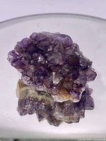Close-up photo of raw amethyst cluster showing purple crystals with mixed mineral inclusions on a reflective surface.