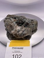 Full view of the raw mineral display piece placed on a round 7 inch mirror to show scale. The mineral features a cluster of dark metallic crystals embedded in quartz.