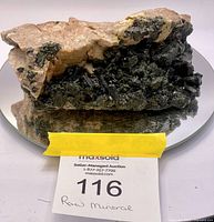 Raw mineral rock placed on a round mirror showing detailed black crystal formations and beige matrix from front angle.