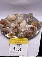 Twelve assorted rough agate and chalcedony mineral specimens arranged on a round mirrored surface showing natural textures and colors.