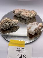 Three raw mineral specimens on a mirrored base showing varied sizes and textures.