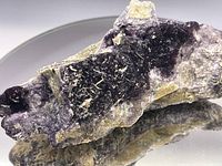 Close-up photo of deep purple raw mineral specimen on a round mirror showing its crystal texture and color variations