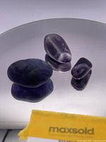 Three tumbled amethyst stones on a reflective surface showing their smooth matte finish and purple color.