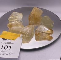 Seven raw tumbled citrine stones arranged on a reflective circular surface, displaying various shades of yellow and amber.