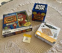 Photo of three sealed games on a lace tablecloth: Press Your Luck board game, STEM Technology educational game, and a small blue box labeled Game Box 'Press Your Luck'.