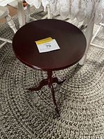 Photo of small dark stained wood round side table or plant stand on a woven rug, showing entire table and tripod base.