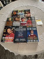 Photo showing 11 Star Trek biographies and novels on a lace covered round table, featuring various authors and characters such as Gene Roddenberry, Leonard Nimoy, George Takei, William Shatner, and Nichelle Nichols.