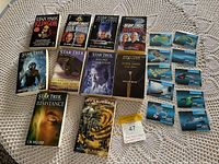 Photo showing 11 Star Trek The Next Generation novels and 13 collectible cards on a crocheted tablecloth.