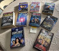 Nine Star Trek paperback novels arranged on a woven textured surface, showing covers and titles.
