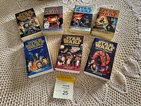 Seven Star Wars paperback novels arranged on a lace tablecloth, showing front covers with characters and scenes from the series.