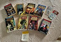Lot display on crocheted tablecloth showing nine Star Wars paperback novels with colorful covers and two sealed Star Wars collectible trading cards.