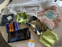 Photo showing all items including silk scarves in various colors and patterns, white tablecloth beneath, and pink lace doily.
