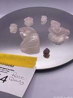 Six tumbled rose quartz stones of various sizes and one small dark purple amethyst crystal point arranged on a reflective surface.