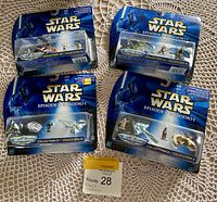 Four sealed packs of vintage Star Wars Micro Machines from Episode I displayed on a lace tablecloth.