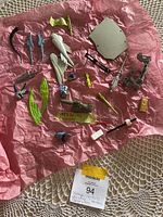 Photo showing an assortment of vintage toy parts including weapons, wings, and other pieces laid out on pink fabric.