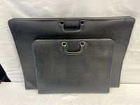 Two black flat portfolio cases, one large and one smaller, stacked with handles visible.