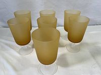 Seven amber frosted glass goblets arranged in a loose group showing their size and shape, frosted texture on bowls and clear stems.