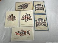 Five handmade art cards spread out showing nature-themed animal designs in black and red formline style on beige background, some with matted blue or beige paper.