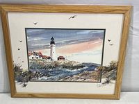 Full view of framed watercolor painting depicting the Portland Headlight lighthouse scene including sky, ocean, rocks, and buildings.