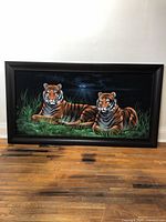 Full view of the black velvet painting showing two tigers in a nighttime grassy setting framed in modern black plastic.