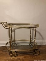 Full side view of brass bar cart showing two-tiered clear glass shelves, gold-tone metal frame with tubular legs and four wheels