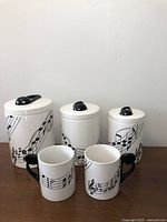 Photo showing full set of three ceramic canisters and two mugs with musical note design