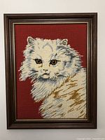 Full view of the framed needlepoint cat artwork showing the entire piece with the wood frame.