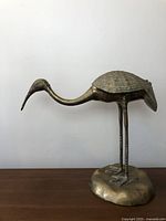 Full side view of the brass bird sculpture showing body and beak shape.