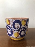 Front view of the vintage German ceramic planter pot showing blue spiral and yellow leaf designs on textured white and brown speckled surface.