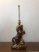Front view of vintage ceramic horse lamp showing the horse rearing on hind legs with curved tail and mane on a base with brown and yellow glaze.