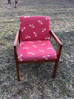 Front view of the wooden chair with red fabric featuring white geometric accents set outdoors on grass.