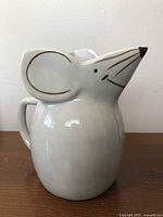 Front-left side view of the ceramic mouse pitcher jug showing the smiling face, ears, and nose spout.