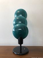Front view of lamp showing three teal glass shades on black metal base