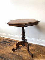Side view of sturdy wooden hexagonal occasional side table showing turned pedestal base and three feet.