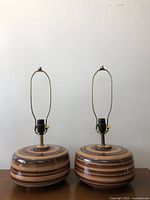 Full view of the pair of brown ceramic lamps with brass fittings on a wooden surface against a plain wall.