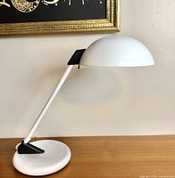 Side angle showing the curved white arm, black accent, and dome-shaped white shade of the lamp on a wooden surface.