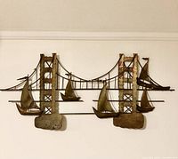 Full view of the brutalist style metal wall art piece depicting sailboats in front of a suspension bridge.
