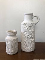 Both Scheurich vases shown side by side on wood surface, white matte glaze with raised patterns